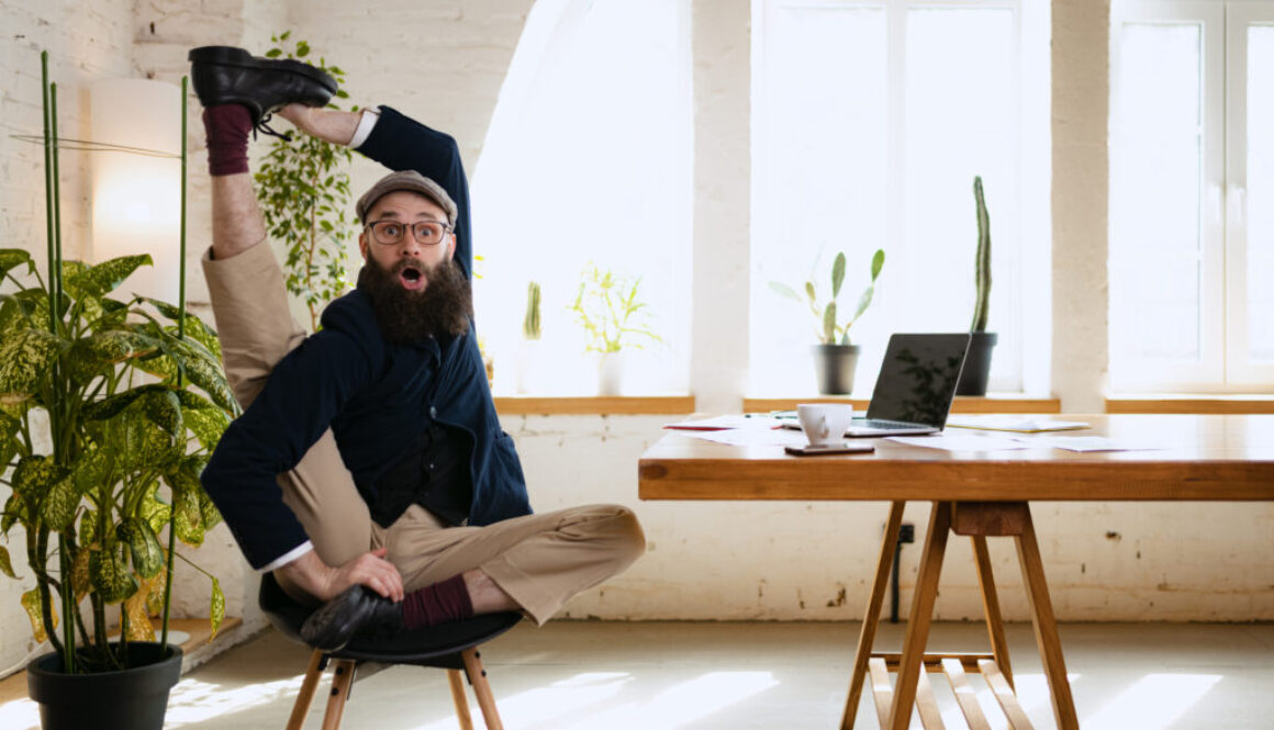 Emotive man stretching his leg at office while working on laptop. Businessman resting